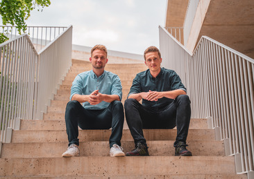 Tobias Dser und Hendrik Sander sitzen auf einer Treppe und blicken in die Kamera